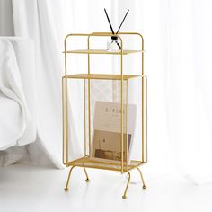 a magazine rack with a book on it in front of a bed and white curtains