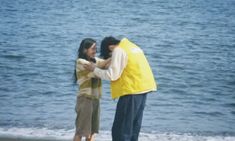 two people are standing on the beach with their arms around each other as they hug