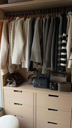 a closet filled with lots of sweaters and handbags on top of wooden drawers