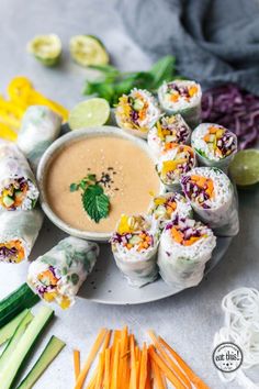 there are many rolls on the plate with dipping sauce and vegetables in the bowl next to it