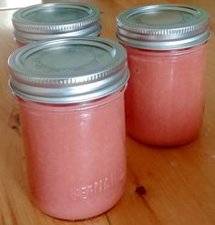 three jars with pink colored liquid sitting on top of a wooden table