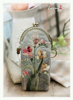 a small purse with flowers on it sitting next to a white vase and other items