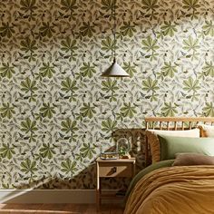 a bed sitting under a lamp next to a wallpaper covered in green and brown leaves