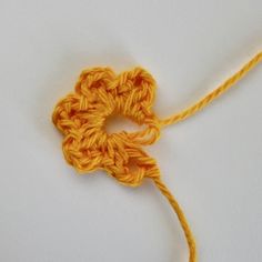 an orange crochet flower is shown on a white surface with yellow yarn in the shape of a heart