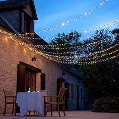 an outdoor dining area with string lights strung over the table and chairs, next to a stone building