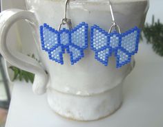 "Be the present with these blue ribbon bows on each side of your face! These adorable blue bows with sparkling darker blue accents are wonderful gifts for any occasion. Exciting and trendy, these earrings will enhance any outfit and will bring many compliments. These earrings are so light that they dance and sparkle with every move you make. Handmade with tiny Miyuki Delica beads they are as unique as they are cute. The sterling silver lever back closures mean you don't have to worry about them slipping out of your earlobe. The dangle's length and the bow's width are close to 1\". AND they are available in several solid colors." Handmade Light Blue Beaded Earrings For Gift, Cute Light Blue Earrings For Gift, Cute Light Blue Earrings Gift, Light Blue Beaded Earrings With Ear Wire As Gift, Light Blue Beaded Earrings Gift, Light Blue Beaded Earrings As Gift, Miyuki Delica Beads, Cute Gifts For Her, Beaded Earrings Diy