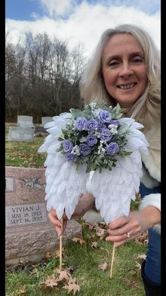 a woman kneeling down next to a grave holding a bouquet of flowers and an angel wing