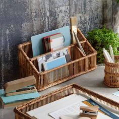 two wicker baskets filled with books and papers on top of a table next to a potted plant