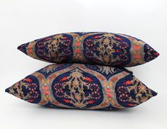 two blue and red decorative pillows sitting side by side on a white surface, one with an ornate design