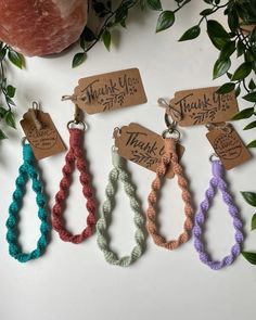 six bracelets with thank you written on them and hanging from the side, next to a plant