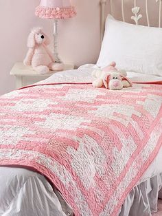 there is a pink and white quilt on the bed with two stuffed animals next to it