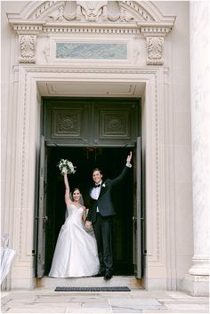 a bride and groom standing in front of a doorway with their arms up to the camera