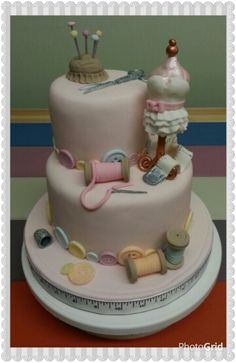 there is a pink cake with sewing items on the top and bottom tiers,