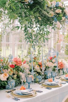 the table is set with blue and white plates, silverware, flowers and greenery