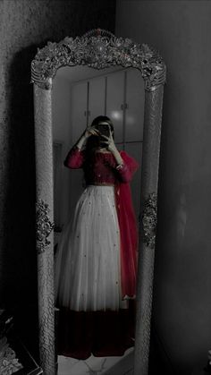 a woman is standing in front of a mirror wearing a dress and holding her hands to her head