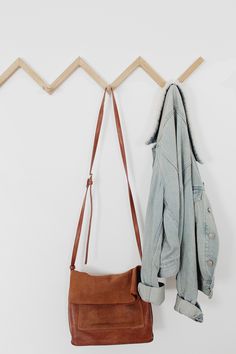 a purse hanging on the wall next to a coat rack and jacket hanger,