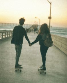 two people are skateboarding on the boardwalk near the ocean at sunset or sunrise time