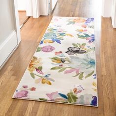 a white rug with colorful flowers on it in the middle of a wooden floored hallway