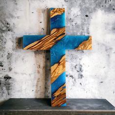 a wooden cross sitting on top of a cement block next to a wall with blue and yellow paint