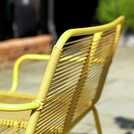 a yellow metal bench sitting on top of a cement floor next to a brick wall