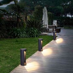 some lights that are on the side of a wooden walkway in front of grass and trees