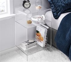 a clear shelf with magazines and an alarm clock on it next to a white bed