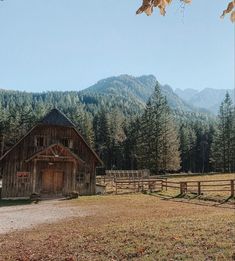 an old barn sits in the middle of a field with mountains in the back ground