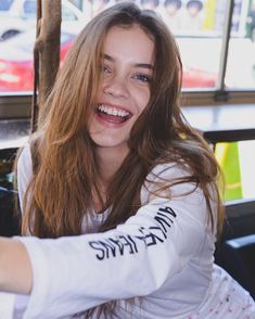 a woman sitting at a table with a pizza in front of her and smiling for the camera