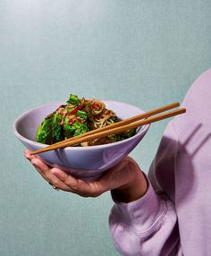 a woman is holding a bowl of food with chopsticks in her left hand