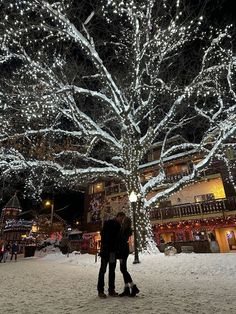 two people standing under a tree covered in lights