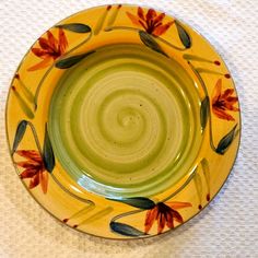 a yellow plate with red and green flowers on it sitting on a white tablecloth