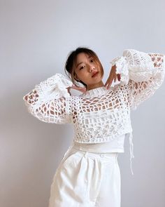 a woman in white is posing with her hands behind her head and she has one hand on her hip