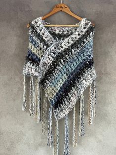 a crocheted shawl with fringes hanging on a hanger against a wall