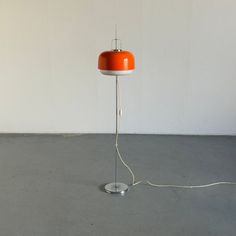 an orange floor lamp with a white base and wire running across the top of it