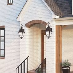 a white brick house with two black lanterns on the front door and stairs leading up to it