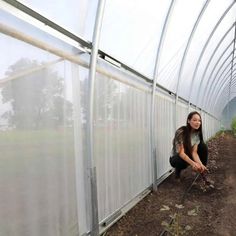 a woman kneeling down in front of a green house with plants growing out of the ground