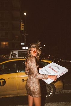 a woman is walking down the street with a pizza box in her hand and sunglasses on