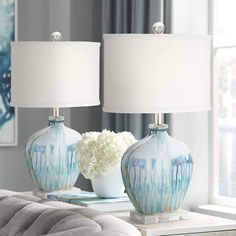 two blue and white vases with flowers on a table in front of a window