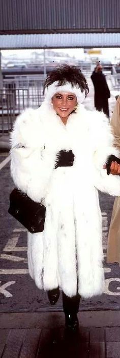 a woman in a white fur coat and black boots is walking through an airport terminal