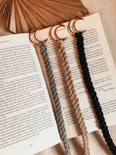 four braided bookmarks sitting on top of an open book next to a fan