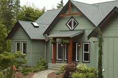 a green house with brown trim and red door, surrounded by greenery and trees