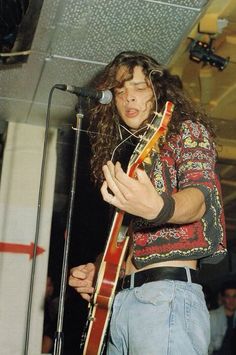 a man with long hair holding a guitar in front of a microphone