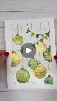 someone holding up a christmas card with ornaments hanging from the top and bottom of it