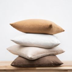 four pillows stacked on top of each other in front of a white wall and wooden table