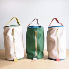 three canvas bags with zippers are lined up on a table, one is green and the other is white