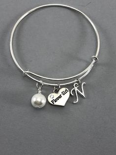 Flower girl charm bangle bracelet with a pearl charm and initial.Features: Adjustable Bangle Bracelet, Silver PlatedMeasures 61mmThe pearl charm is made from a zinc alloy metal which is lead and nickel free.Measurements: 18mm x 15mmEach purchase will arrive packaged in a cute kraft gift box ready to give as a present or a fun gift for yourself!Add on a birthstone charm for $3.00Additional add on charms or initial charms $3.00https://www.etsy.com/shop/OurLittleCharms?ref=hdr_shop_menu&section_id= Pearl Wedding Jewelry, Flower Girl Proposal, Wife Jewelry, Flower Girl Bracelets, Girl Bracelet, Bracelet Flower, Adjustable Bangle Bracelet, Pearl Jewelry Wedding, Gift Flower