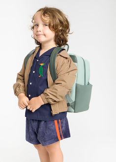 a little boy with a backpack standing in front of a white background and looking at the camera