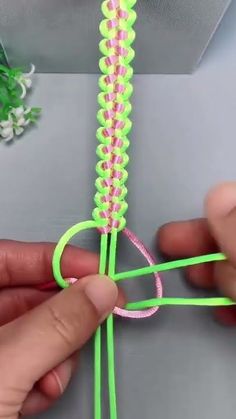 someone is making something with neon green and pink thread, while another person holds the string in their hand