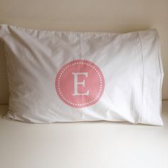 a white pillow with a pink monogrammed letter e on it sitting on a bed