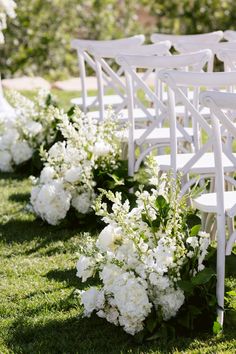 rows of white chairs with flowers on them in the grass at an outdoor wedding ceremony